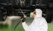 Person applying Corrosion-Free Oil Guard on underside of vehicle